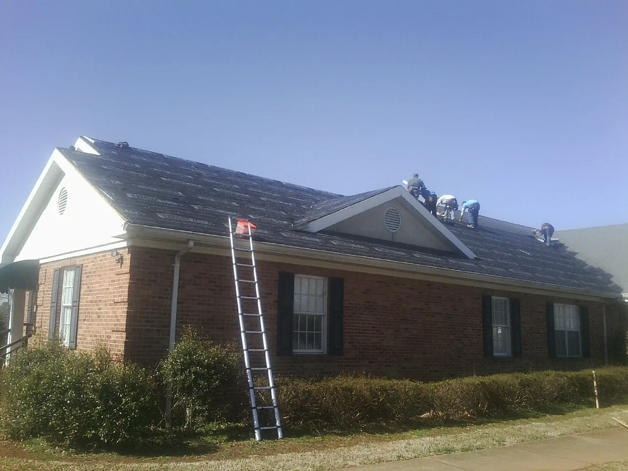 Crew tearing shingles off a brick ranch roof with a ladder set — Emergency Roof Repair work by our crew in Lyndora