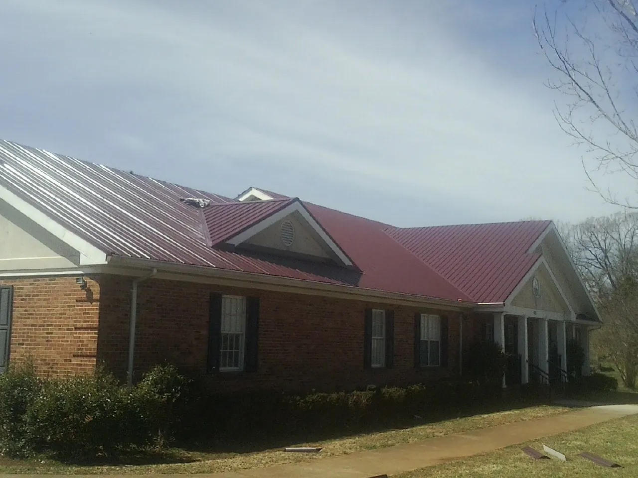 Red metal roof with gabled entries on a long brick building, from a Hail Damage Roof Repair job in Lyndora