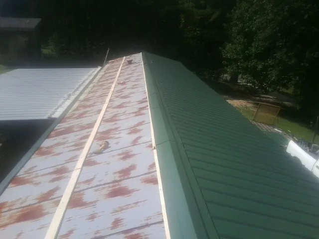 Old rusted panels beside newly installed green metal roofing — Wind Damage Roof Repair by Roofing Brothers in Lyndora