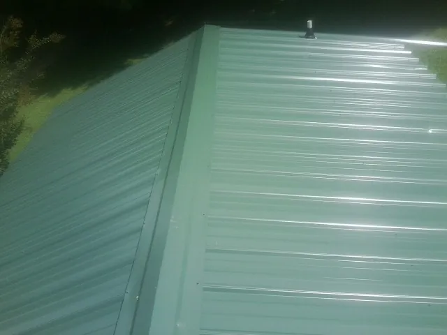 New green metal panels meeting at the ridge of a roof — Flat Roof Repair work by our crew in Lyndora