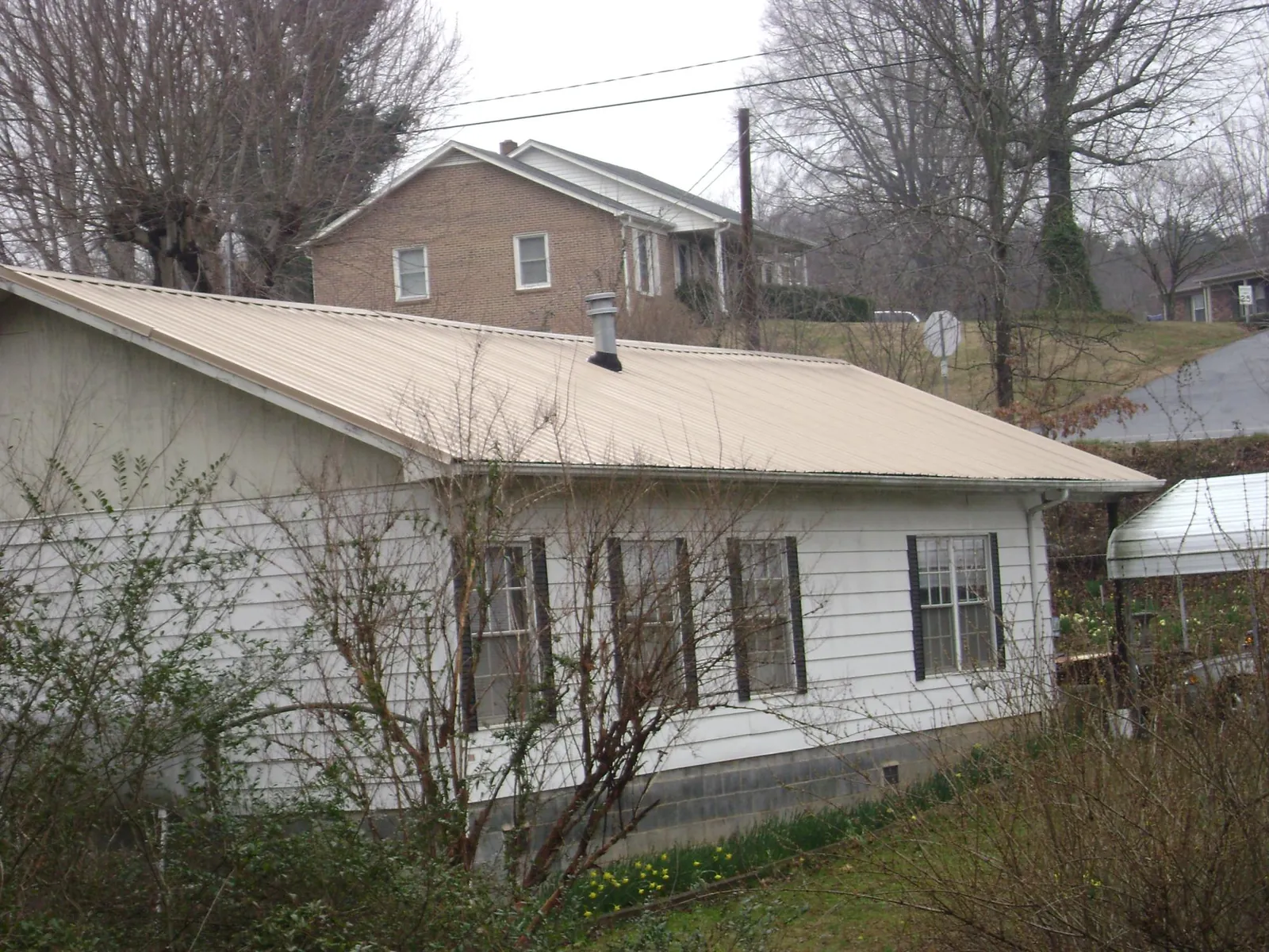 Tan metal roof on a white sided house set into a hillside — Commercial Roofing by Roofing Brothers in Lyndora